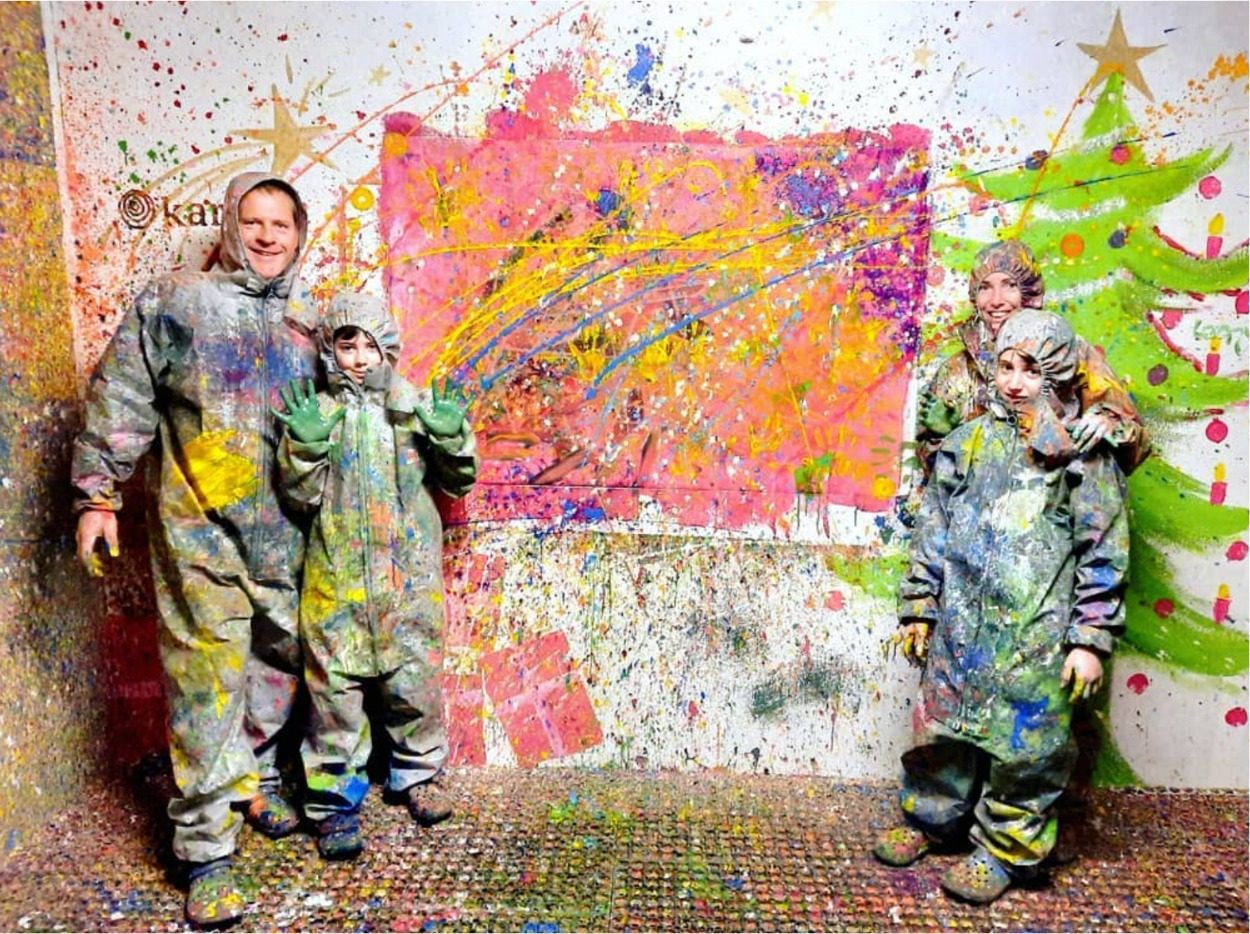 Tagraum: Gruppe im Overall vor einer mit Farbe bespritzten Leinwand, beleuchteter Raum